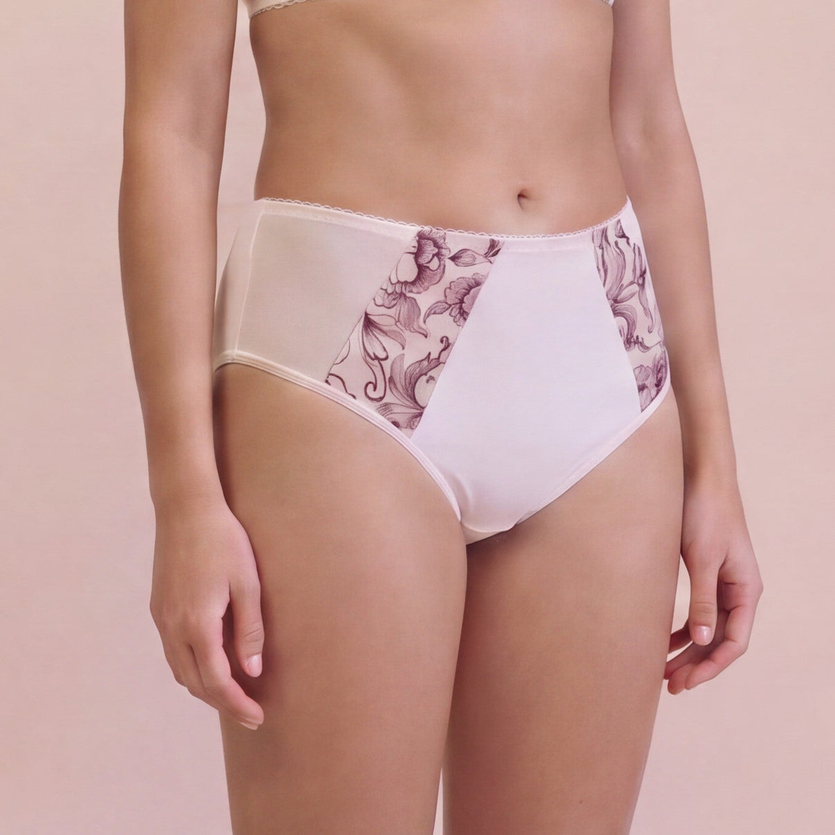 A model wearing high-waisted light beige underwear with mauve floral patterned side panels, shown from the waist to upper thighs against a solid pale pink background.